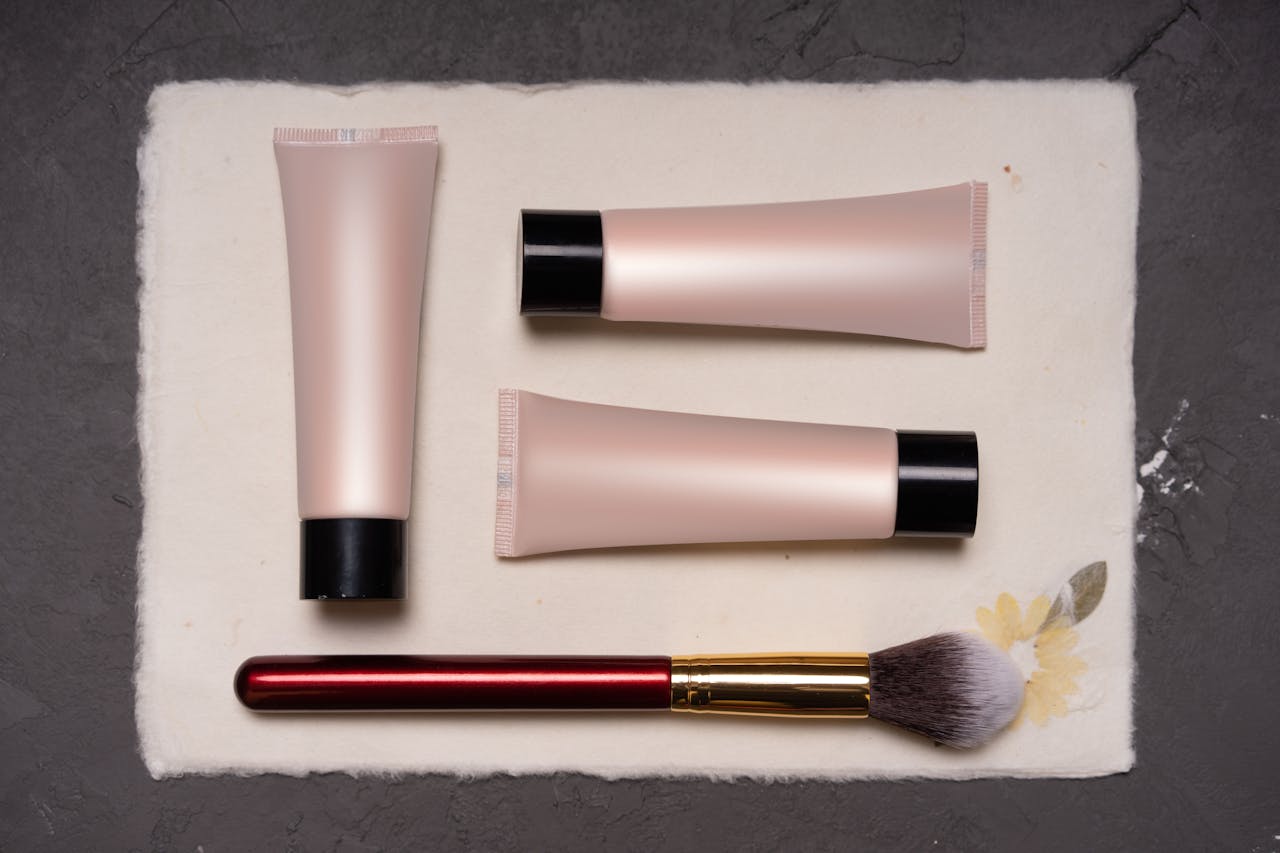 Beauty composition featuring cosmetic tubes and a makeup brush on a textured background.